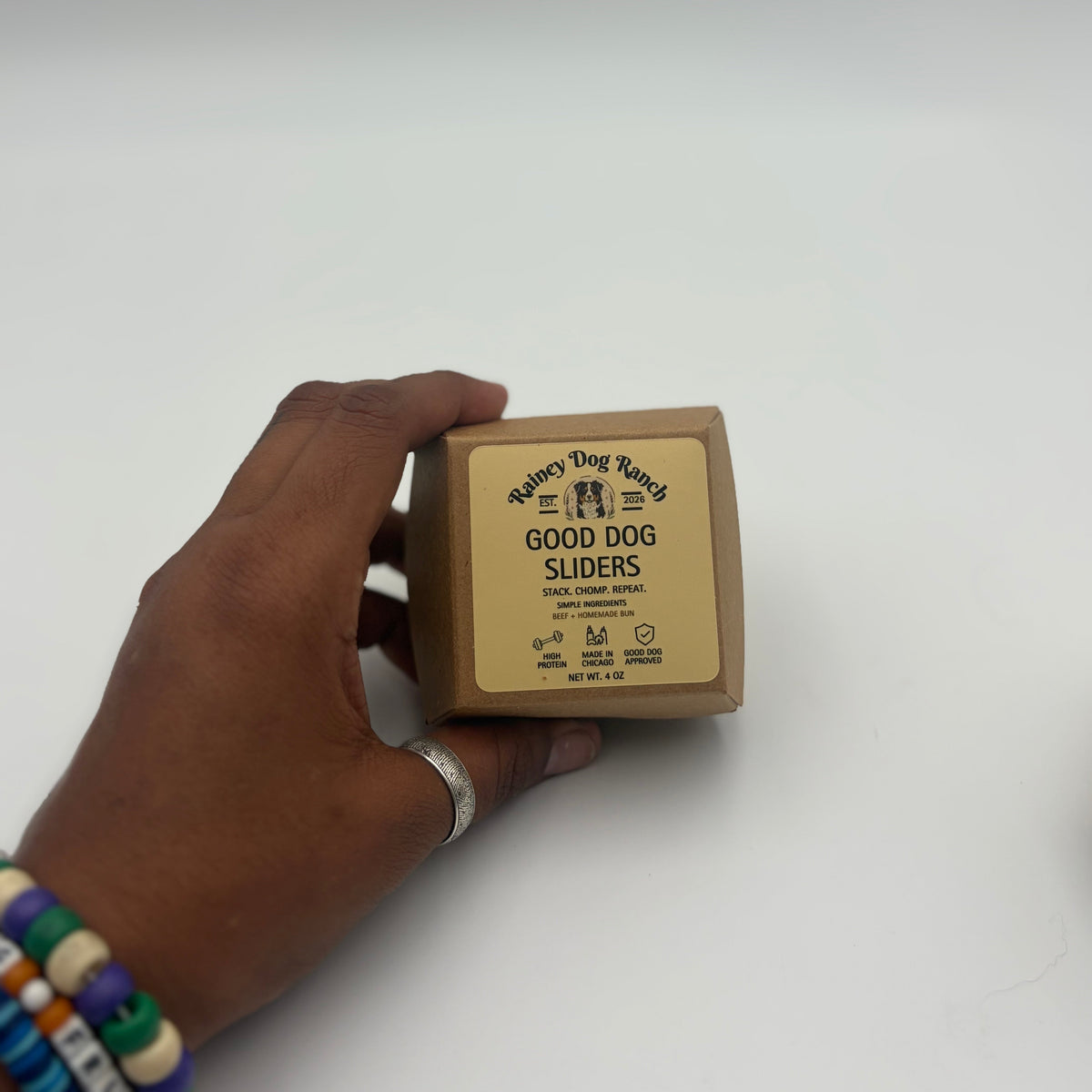 A hand holding a square cardboard box of 'Good Dog Sliders' by Rainey Dog Ranch against a plain white background.