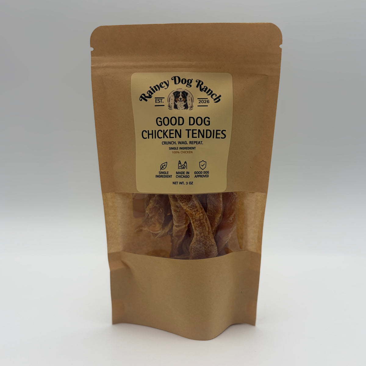 A stand-up kraft paper pouch of Rainey Dog Ranch Good Dog Chicken Tendies, featuring a clear window that shows the dried chicken tendies inside, set against a neutral gray background.